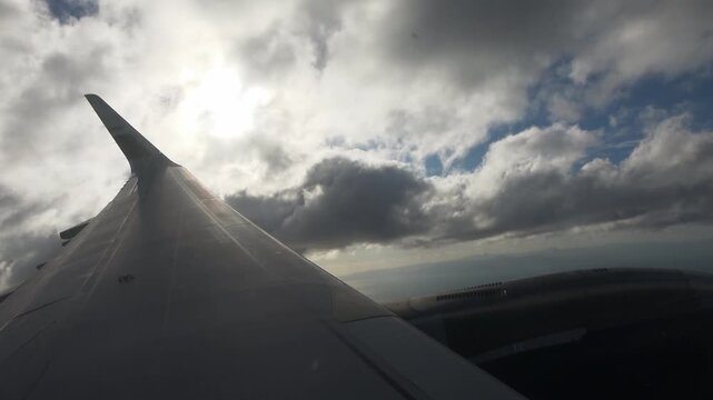 An airplane wing through a cabin window, flying below the clouds and over the ocean.