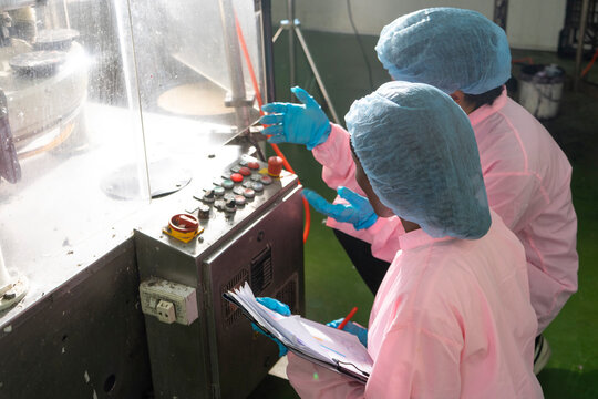 Asian male and black woman factory workers monitoring cold drink bottles on production line at drinks production plant.