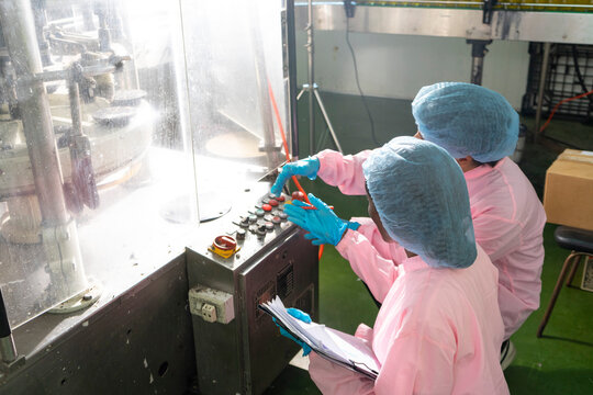 Asian male and black woman factory workers monitoring cold drink bottles on production line at drinks production plant.