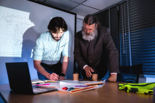 Engineer supervisor and Senior business professionals are discussing strategic building construction project planning in dimly lit office at night. Concept of project planning and schedule.