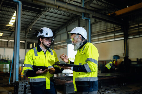 Senior engineer explaining industrial operations to younger colleague in manufacturing facility. Concept of corporate engineering leadership, corporate cooperation, industrial quality control audit.