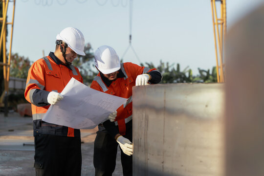Engineers in hardhats inspect steel pipe with blueprint at fabrication outdoor factory yard. Concept of infrastructure development, quality control and engineering management.