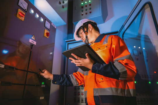Asian young electrical engineers focus control panel symbols and uses tablet to study circuit diagrams for control circuit breakers on the building.