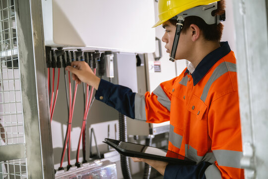 Young asian technician using tablet tracking solar power electrical circuit, checking industrial wiring setup with tablet, checking electric lines on alternative energy board
