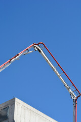 A low angle view of a white and red concrete pump boom arm extending high into the blue sky above a concrete building construction site. © nahhan