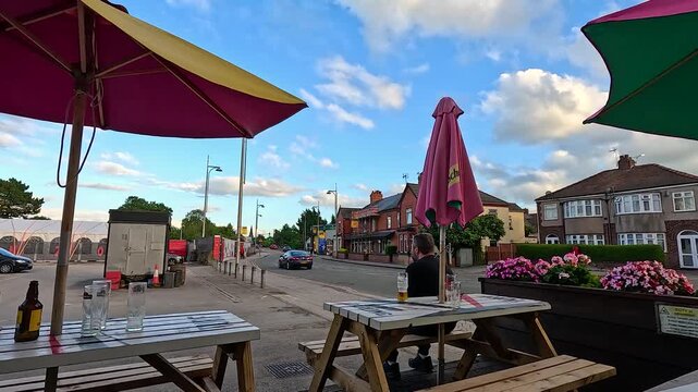 Outdoor pub garden seating with colorful umbrellas and person sitting at wooden table during sunset.
