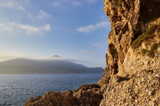 A rocky coast with sea and a mountain in the background, morning light, Tsichli Babas islet, Navarino Bay, Pylos, Peloponnese, Greece