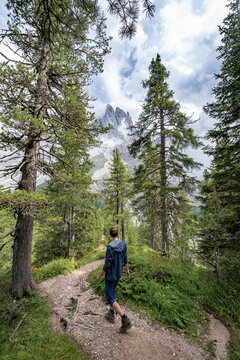 Young man, hiker on a hiking trail in the forest, in the back mountain peaks of the Geislergruppe, Parco Naturale Puez Odle, South Tyrol, Italy