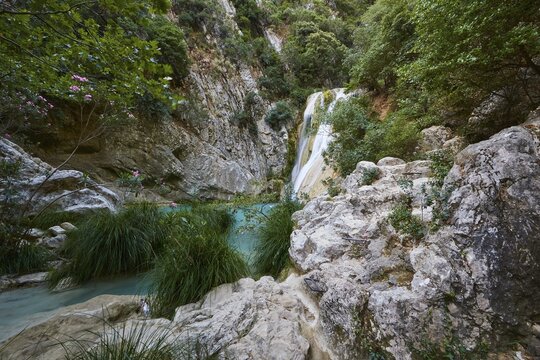 A waterfall surrounded by lush vegetation and rocks flows into turquoise water, waterfalls, ponds, Polylimnio, Peloponnese, Greece