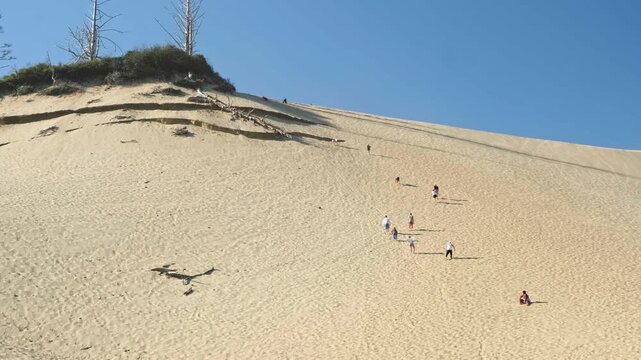 People climbing up the steep sandy slope of the giant sand dune at Cape Kiwanda, Oregon