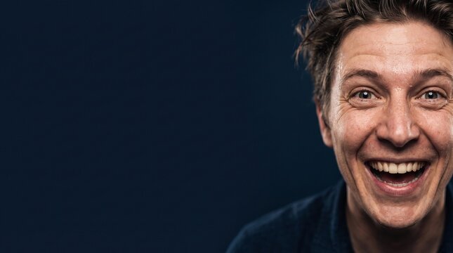 Close-up portrait of an ecstatic man with an expressive wide smile and joyful facial expression against a dark blue background
