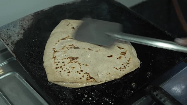 Close up of cooking rotti or chapati on a hot flat iron griddle (tawa) with a spatula