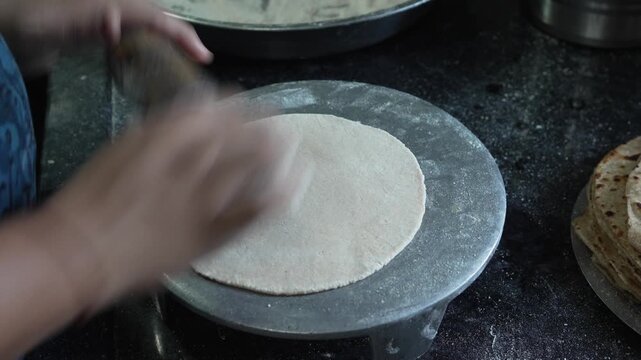 Close up of hands rolling out wheat flour dough with a rolling pin (belan) on a chakla to make roti