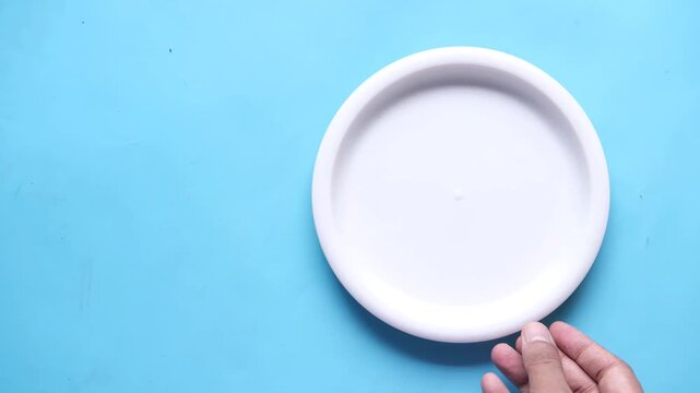 Hand placing light blue plastic disc on bright blue background top view slow motion