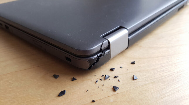 Broken laptop hinge showing plastic fragments on a wooden desk, symbolizing damage and the need for computer repair