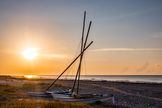 Bright sunrise and golden light illuminating catamaran sailboats resting on the sandy shore at Isle of Palms in South Carolina