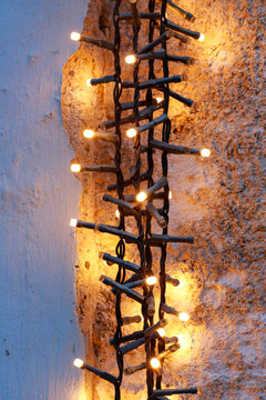 A braided strand of warm fairy lights glowing against a textured wall. Festive Christmas illumination, cozy winter decoration, and seasonal background for holiday greetings.