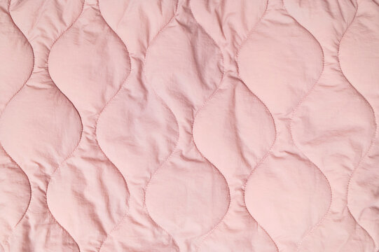 Pink quilted textile shows rounded stitched sections across soft padded material. Fabric texture supports blanket, jacket and clothing concepts, while delicate tone fits fashion and home decor.