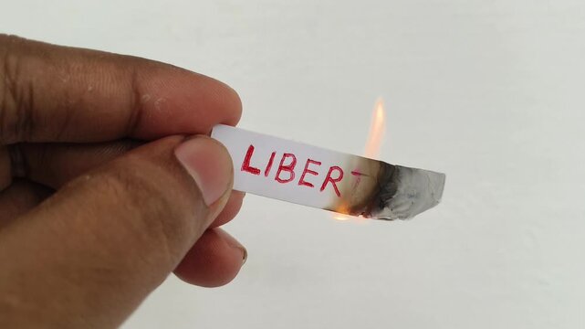 Closeup of hand holding white paper note with liberty word or text written on the surface with burning fire flame. Symbolic concept of citizen person protest against bad government or system failure.