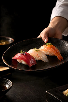 Chef serving assorted nigiri sushi on a black plate