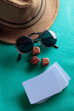 Playing cards, wooden dice, sunglasses and a hat on a green cloth.