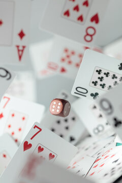 Wooden die in motion surrounded by playing cards.