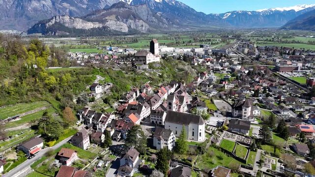 sargans castle bergfried tower hilltop overlooks old town rooftops church spire green farmland snowcapped alpine peaks backdrop rhine valley switzerland aerial panorama drone footage heritage site
