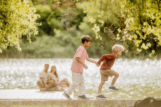 Two joyful boys playfully running by a sparkling lake during a sunny afternoon