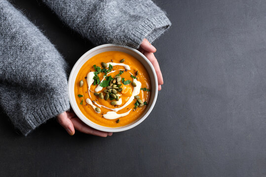 Female hands in knitted sweater holding bowl with pumpkin soup