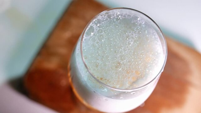 A slow zoom-in reveals a glass of beer on a wooden board. Bubbles burst in the dense foam of the beer. A glass of draft beer on the table. A bar table. POV: drinking beer.
