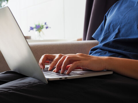 Hands typing on laptop keyboard on lap in relaxed home setting with soft light and casual clothing, conveying focused remote work and quiet concentration