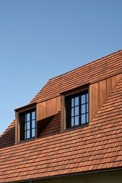Modern roof design with red clay tiles and dormer windows against blue sky