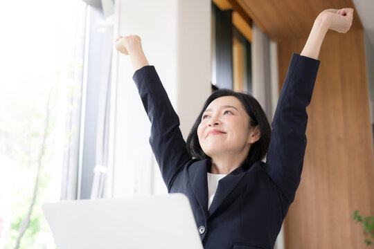 A female office worker doing stretches for stiff shoulders during a break at work; a middle-aged businesswoman refreshing herself in the office. An image of health-conscious management.