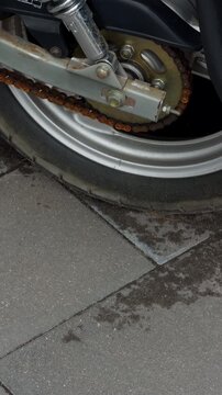Close up of rusty motorcycle rear chain, wheel hub, swingarm, and tire on paved street