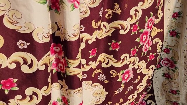 Curtains featuring ornate floral patterns and rich maroon drapes add traditional elegance and warmth to the interior space of a classic residential living room setting.