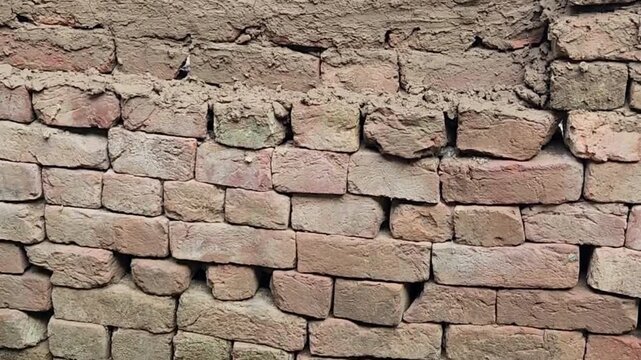 Brickwall displays weathered red clay bricks stacked unevenly with crumbling mortar joints forming an aged rustic surface in an industrial yard environment.