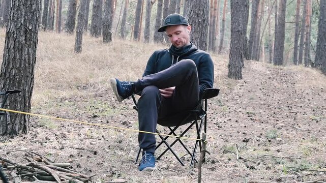 Relaxed young man resting in a portable camp chair in a serene pine forest during outdoor recreation