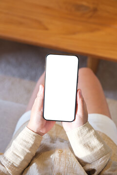 Top view mockup image of a woman holding and using mobile phone with blank desktop white screen at home
