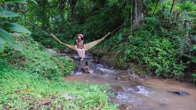 A woman sitting and relaxing in wooden hammock in the creek