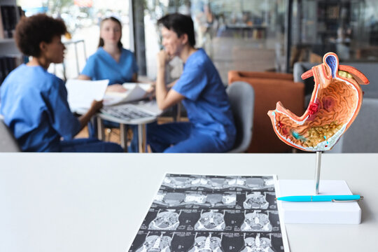 Sectional stomach replica illustrating mucosal inflammation and computed tomography sheets with interns conferring at a study table