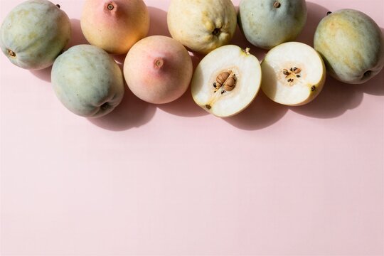 Flat lay of fresh white sapote fruits whole and halved on a pastel pink background with copy space
