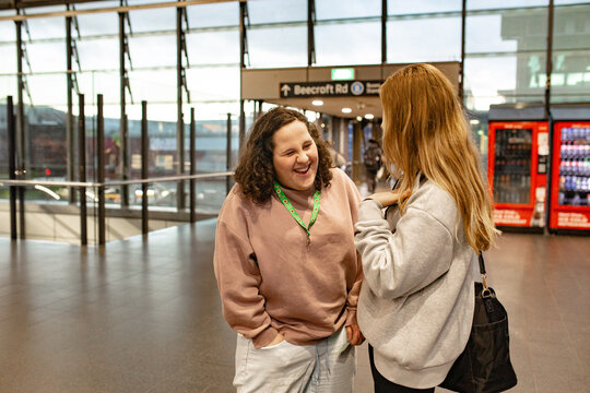 Two young women laughing together and sharing a playful joke inside a busy metro station