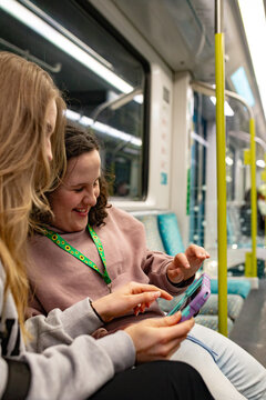 Young woman sitting beside a teenage girl with curly hair holding a tablet on a patterned train seat