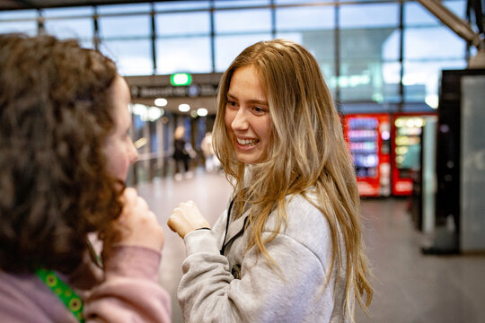 Two young women playfully teasing each other and sharing a laugh inside a busy metro station
