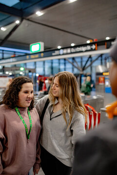 Teen girl and support worker talking with transport staff inside busy train station