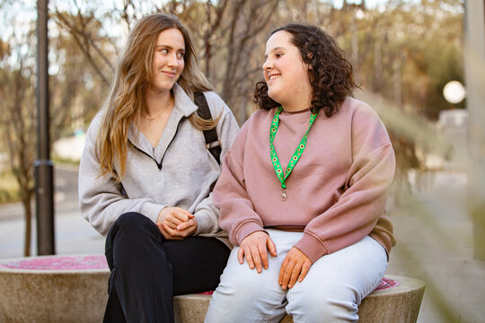 Two ladies teen and support worker sitting and having warm conversation in urban area