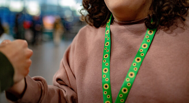 Close-up of a teen wearing a green sunflower lanyard, greeting a person with a friendly fist bump