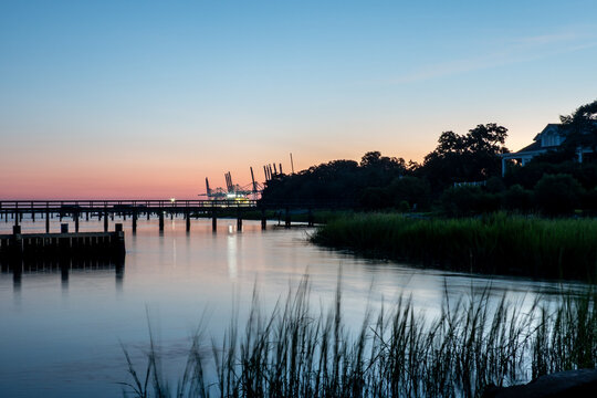 Port container cranes and historic wooden piers silhouetted against the evening sky across the harbor in Charleston South Carolina