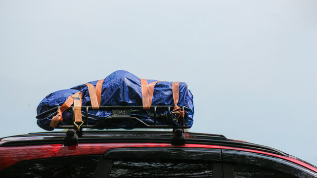 Blue waterproof cargo bag strapped to vehicle roof rack for road trip.