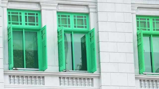 Close up of green wooden shutter windows on historic white building facade in Singapore.